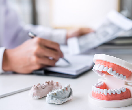 closeup of models of teeth sitting on a dentist's desk while he writes notes in the background